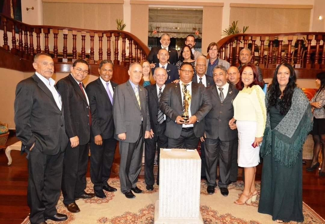 Registro de encontro institucional, com participantes reunidos e um troféu ao centro.
